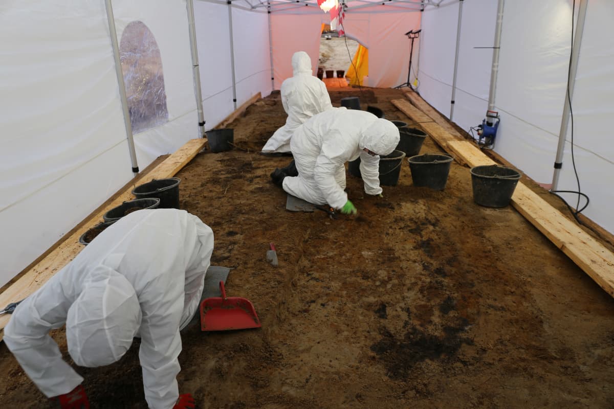 Arkeologit kaivavat maata teltan sisällä.