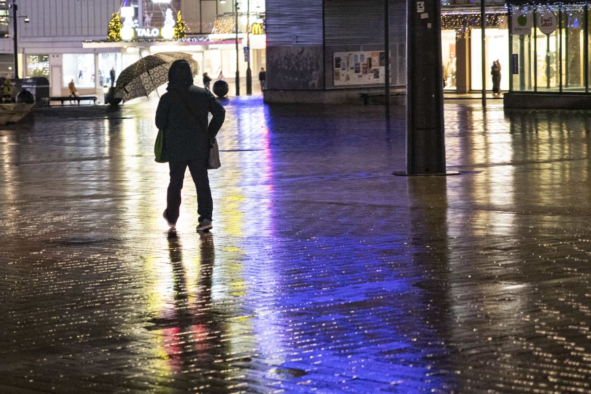 Ihminen kävelee sateenvarjon kanssa sateiselle Kuopion torilla.