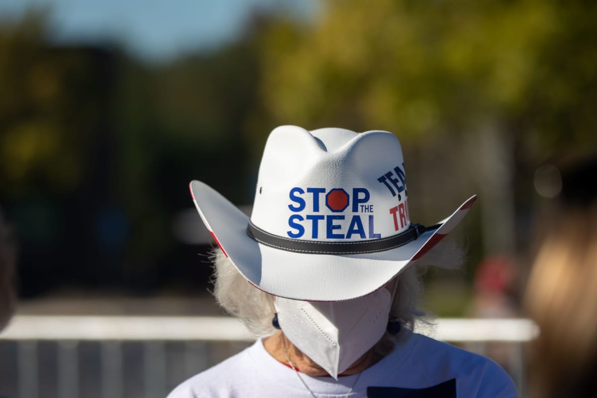 Cowboy hattuinen Trumpia kannattava nainen kasvomaskissa. Valkoisessa hatussa lukee englanniksi: Stop the steal. 