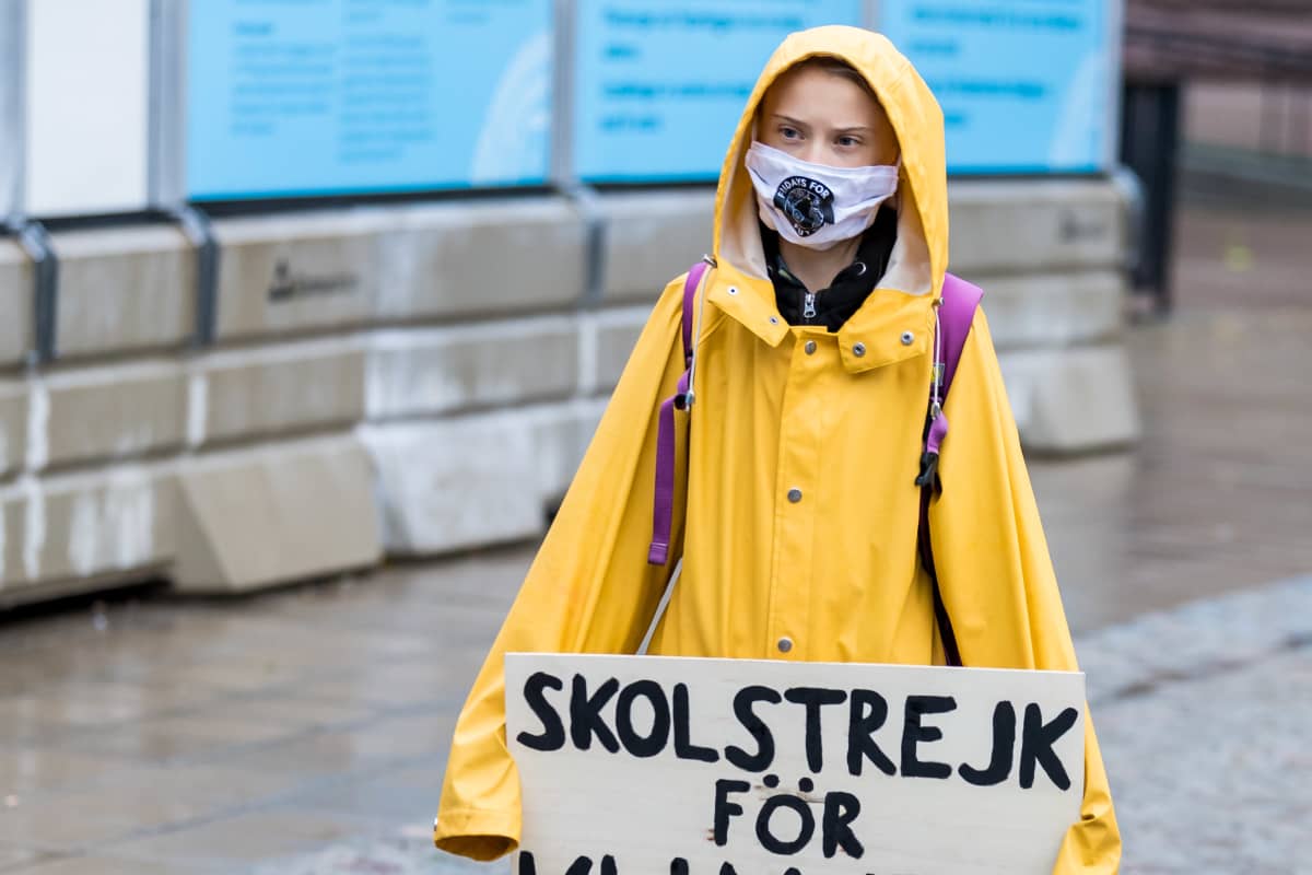 Greta Thunberg keltaisessa sadetakissa ja maski kasvoillaan.