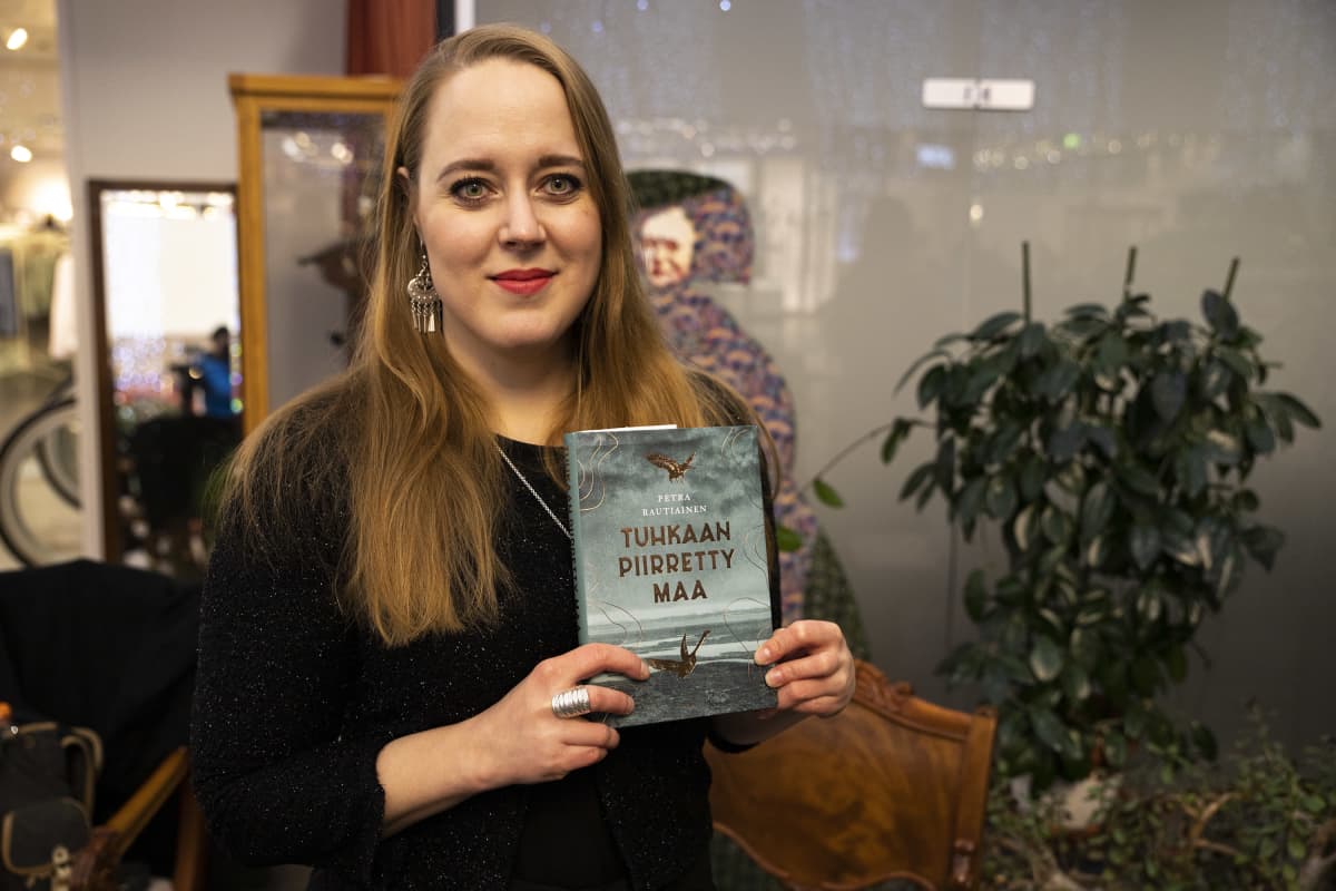 Kirjailija Petra Rautiainen kädessään hänen Savonia-palkittu esikoisteoksensa Tuhkaan piirretty maa.
