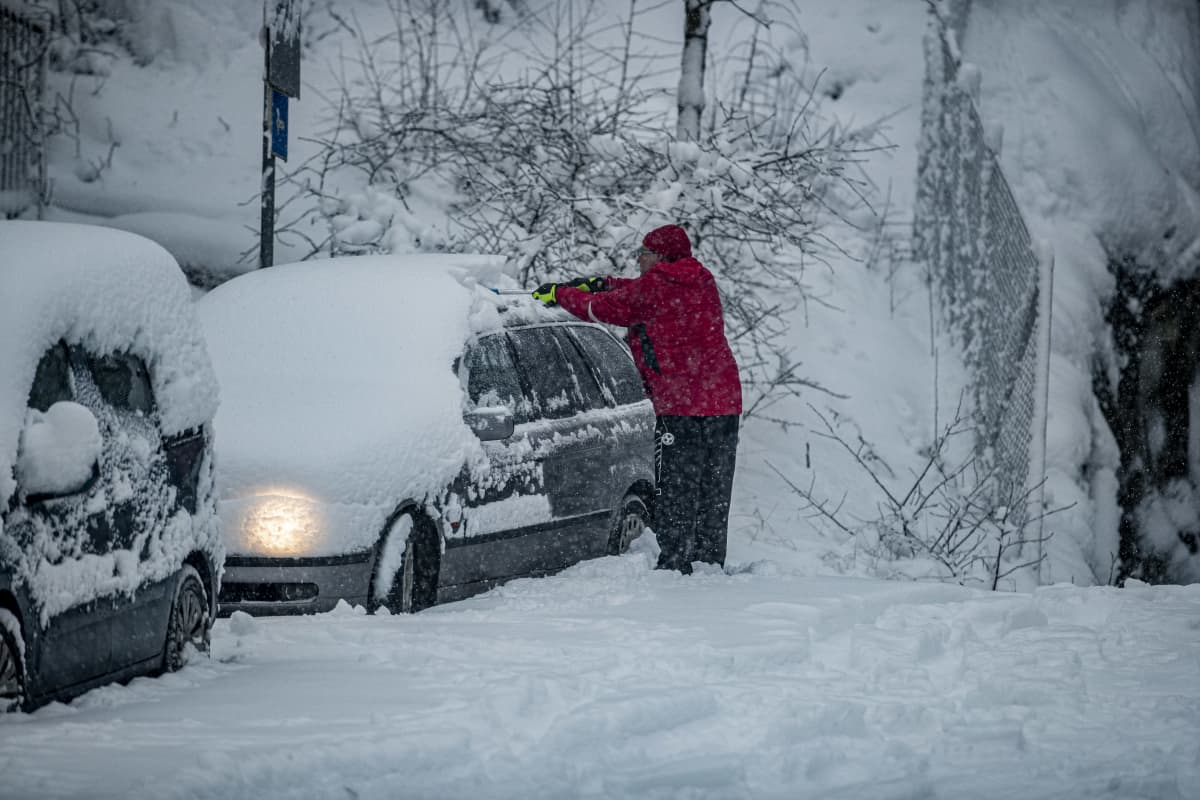 Henkilö putsaa autoa lumesta.