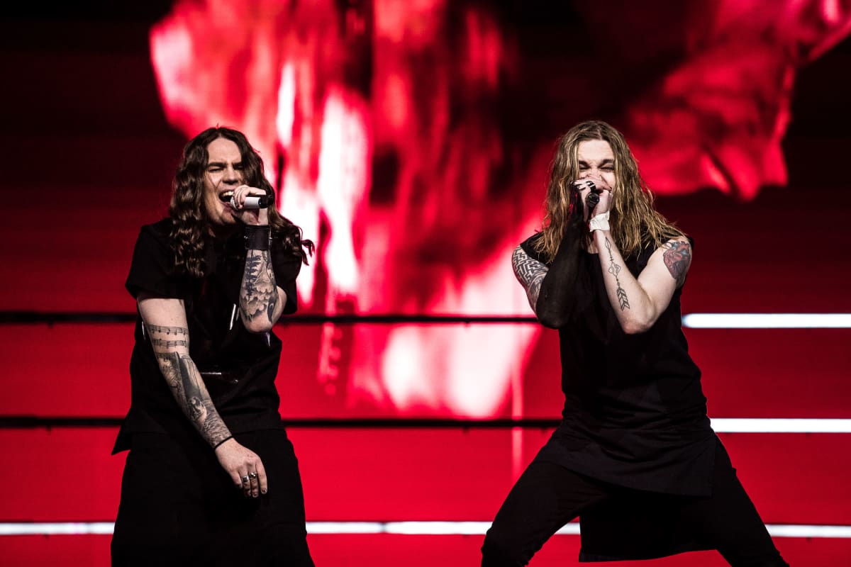 Kaksi Blind Channelin jäsentä laulaa mikrofoniin lavalla, takana voimakas punainen tausta. Molemmilla miehillä on pitkät hiukset ja mustat asut.