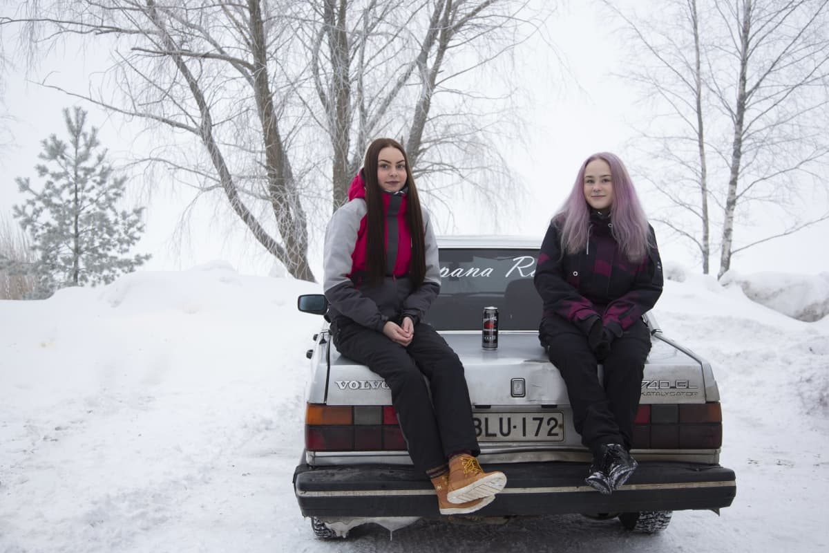 Jenni Herrala ja Sofia Hurtta istumassa Volvon takakontin päällä.