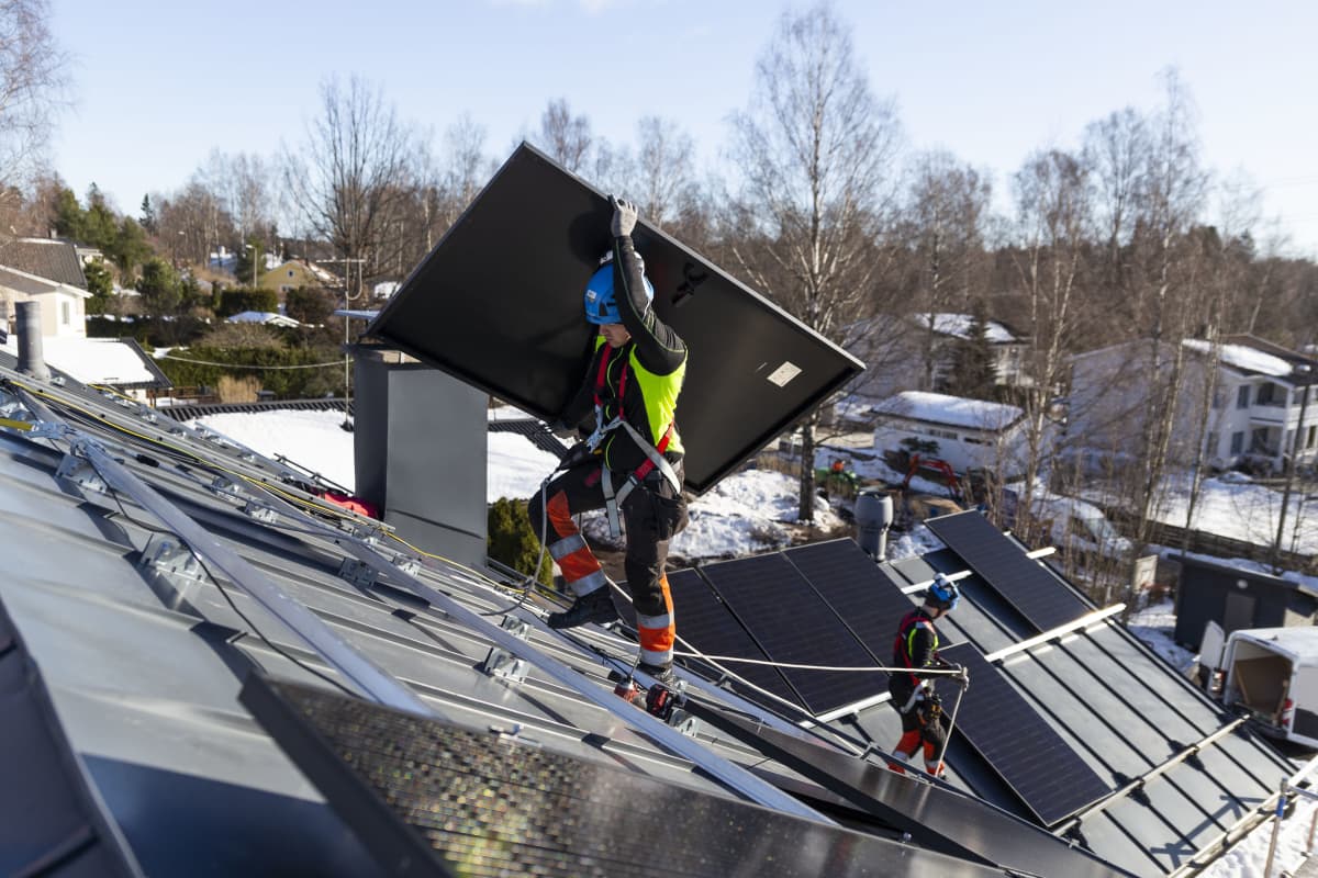 Solarvoima Oy:n asentaja Joni Särkinen kantaa aurinkopaneeleja omakotitalon katolle.