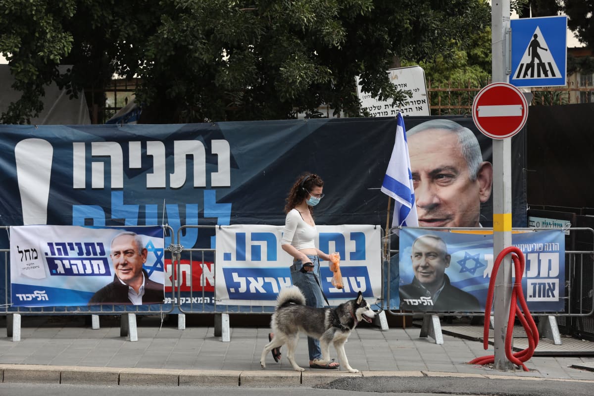 En kvinna med munskydd vandrar i Jerusalem förbi valaffischer föreställande Benjamin Netanyahu.