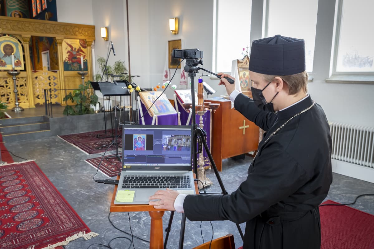 Pappi kokeilee kameraa ja tietokonetta kirkkosalissa etäjumalanpalvelusta varten