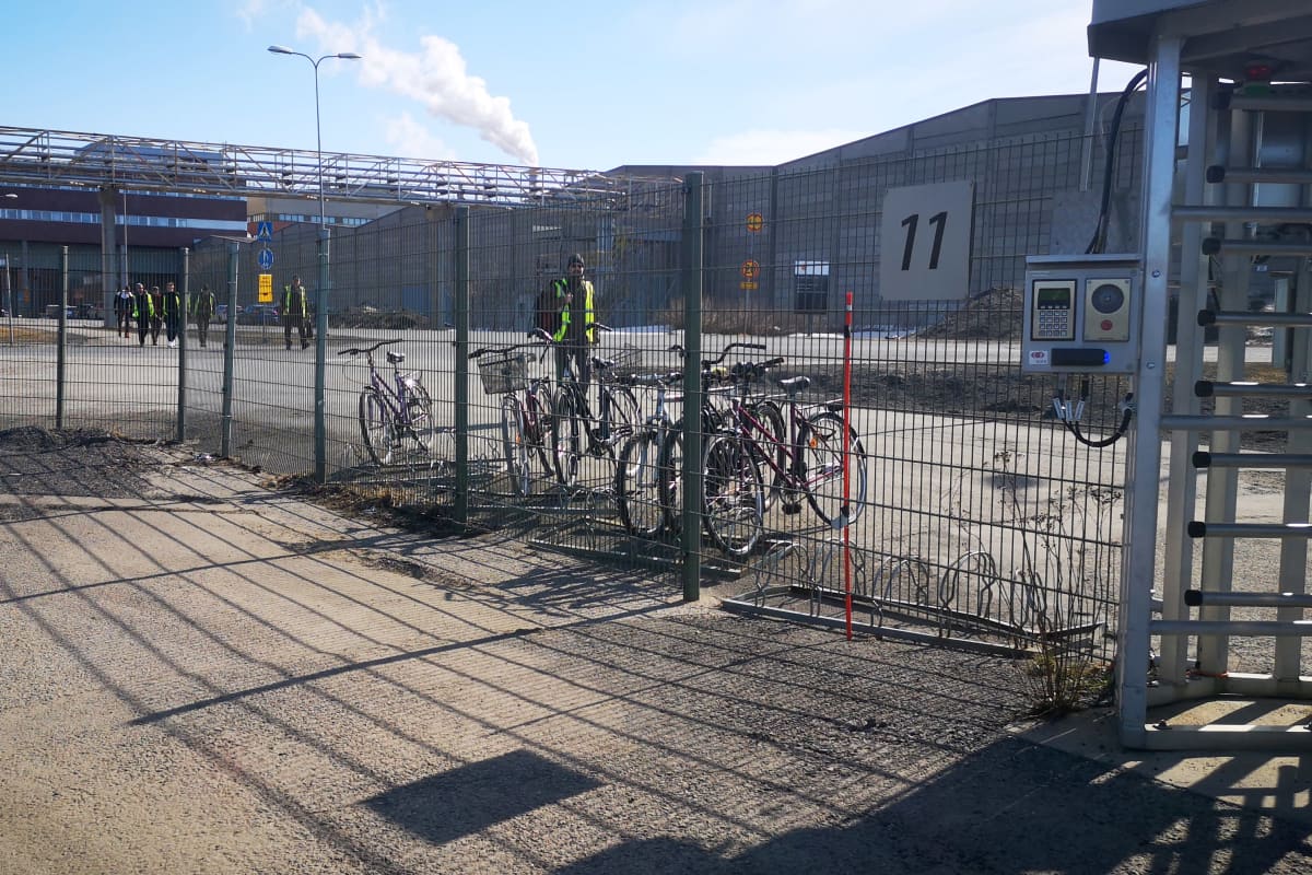 Stora Enson Veitsiluodon tehtaan aita. Aidan takana marssii harvassa jonossa työntekijöitä porttia kohti huomiovärisissä liiveissä.