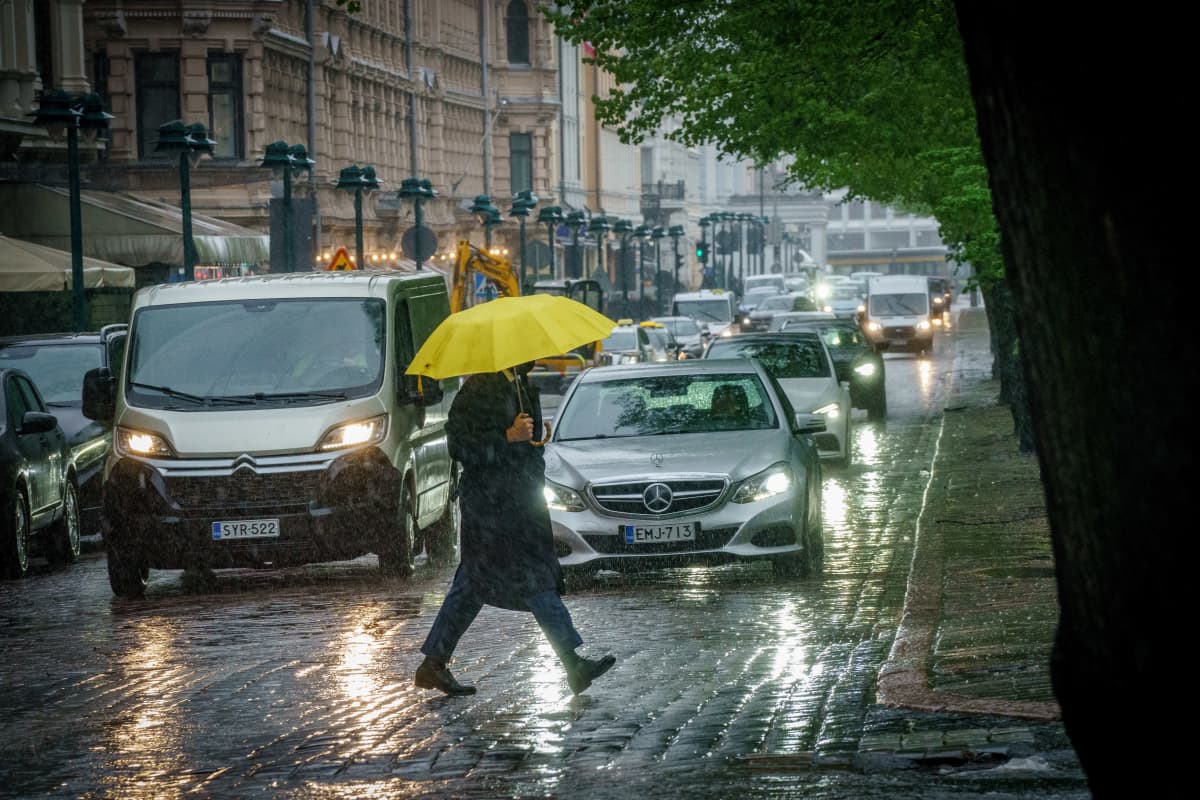 Mies ylittää sateessa suojatietä sateenvarjo kädessään.