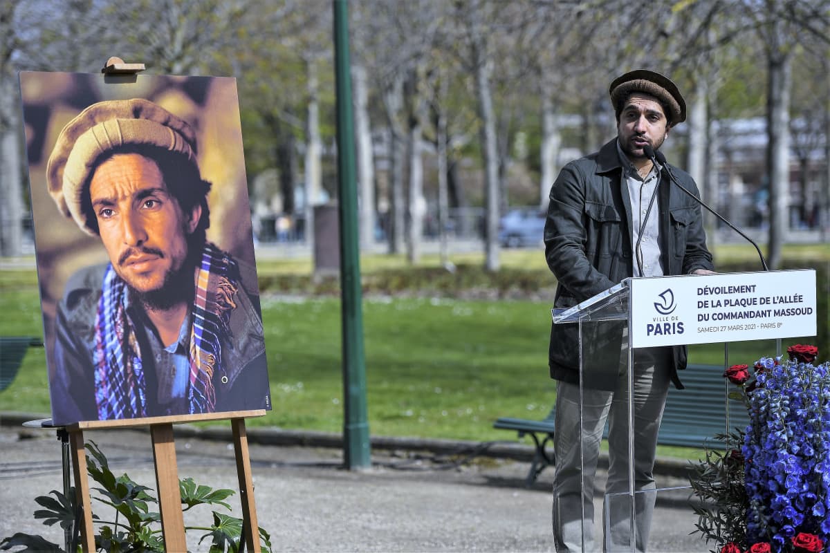 Ahmad Massoud puhuu puistossa puhujanpöntön takana, päässään perinteinen päähine, Vieressä on maalaus hänen isästään.