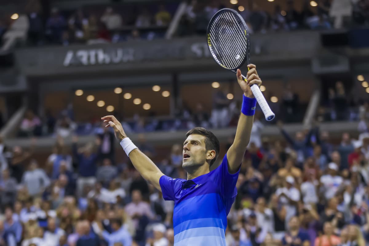 Novak Djokovic lyfter upp sin tennisracket och båda händerna och firar vinst i match.