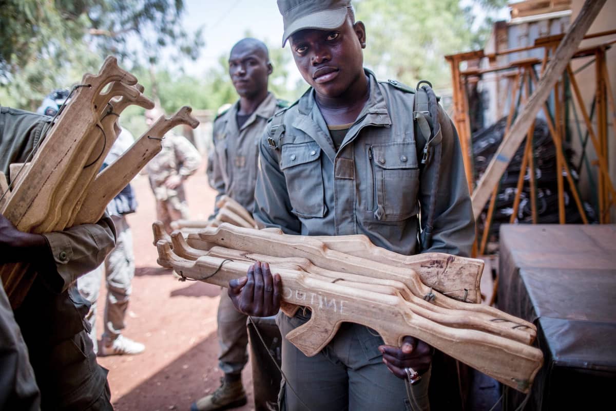 Malilainen sotilas pitelee käsissään puusta tehtyjä rynnäkkökiväärejä.