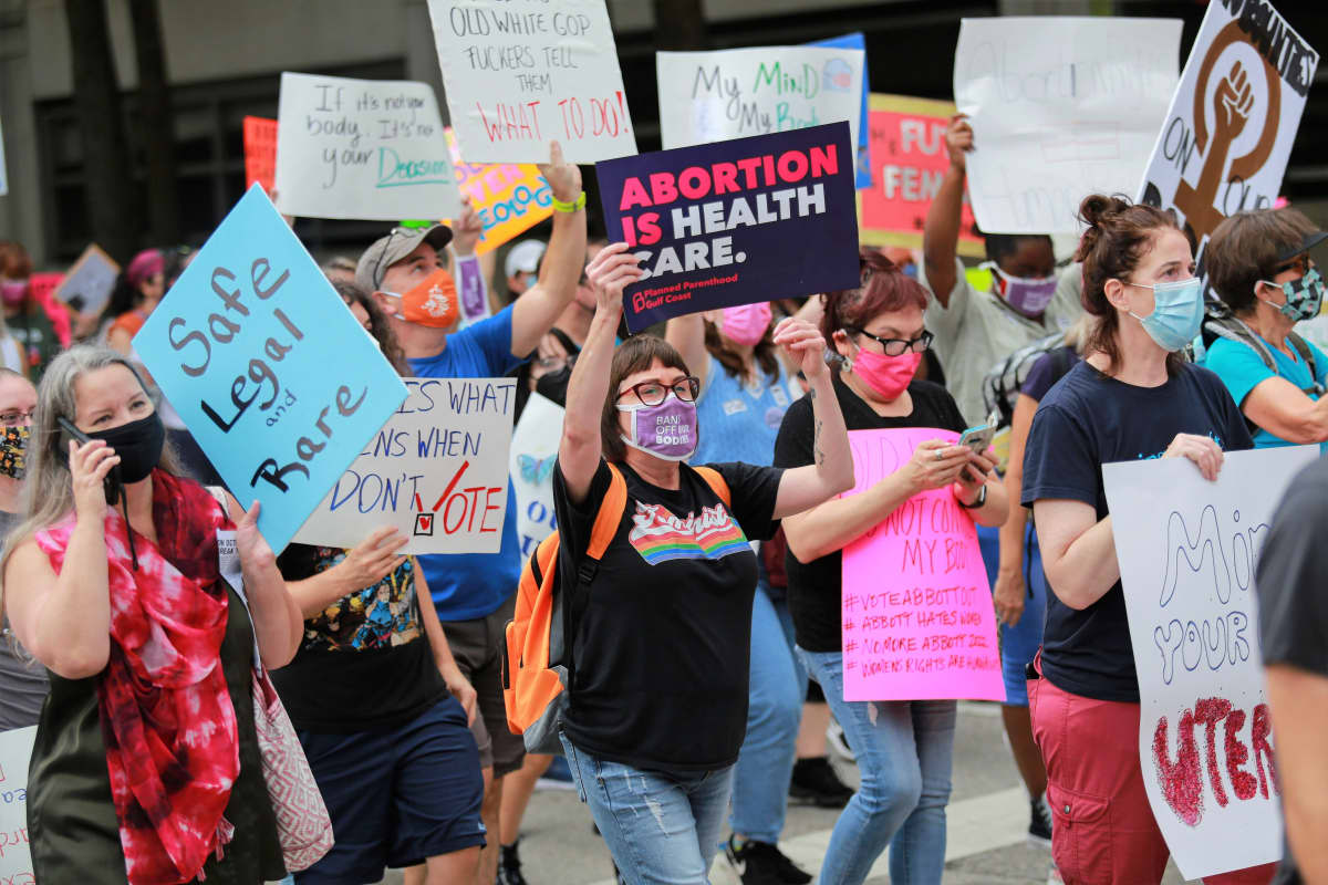 Joukko naisia kulkee plakaattien kanssa. Keskellä kuvaa nainen pitelee kylttiä, jossa lukee englanniksi: "Abortti on terveydenhuoltoa."