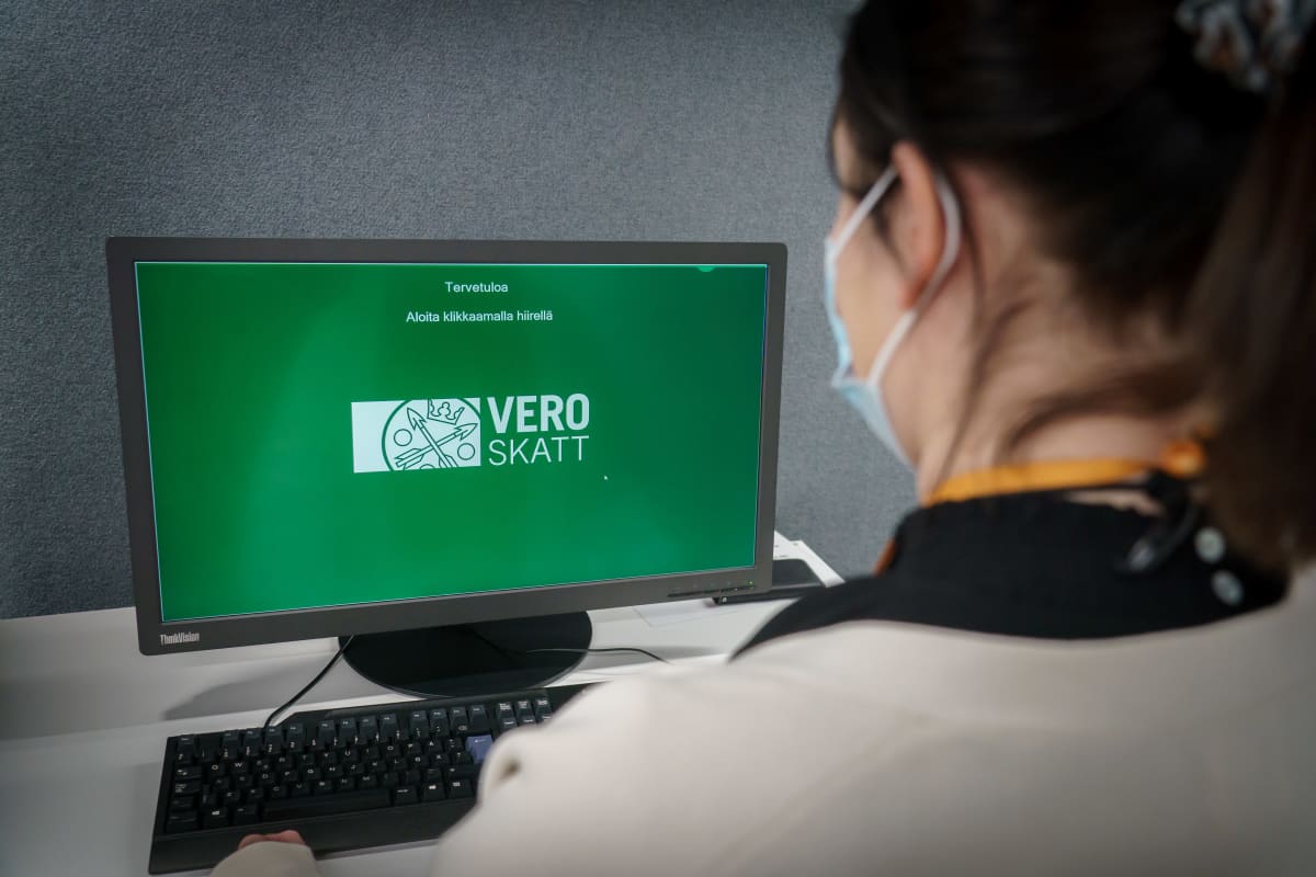 Naishenkilö verotoimistossa käyttämässä tietokonetta, jonka vihreällä näytöllä näkyy verohallinnon logo.