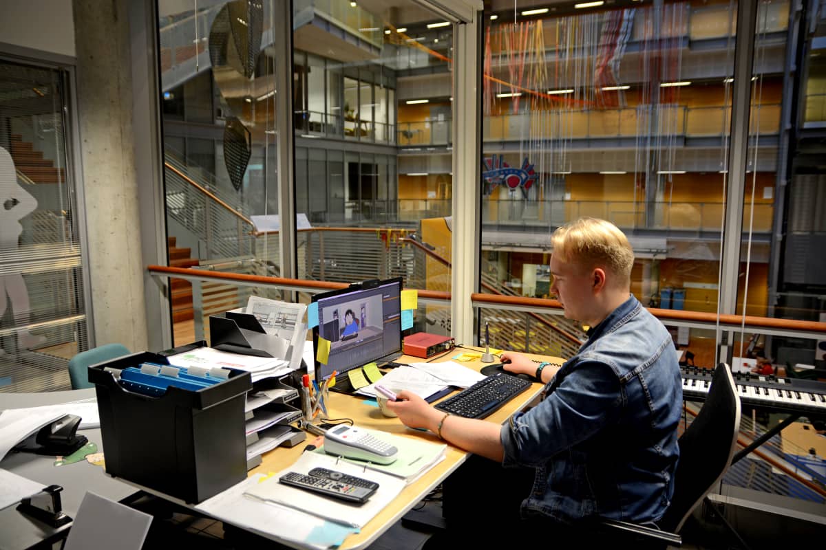 Animaation tekijä Tuomas Toivainen istuu tietokoneen äärellä, taustalla yliopiston lasinen sisäseinä.