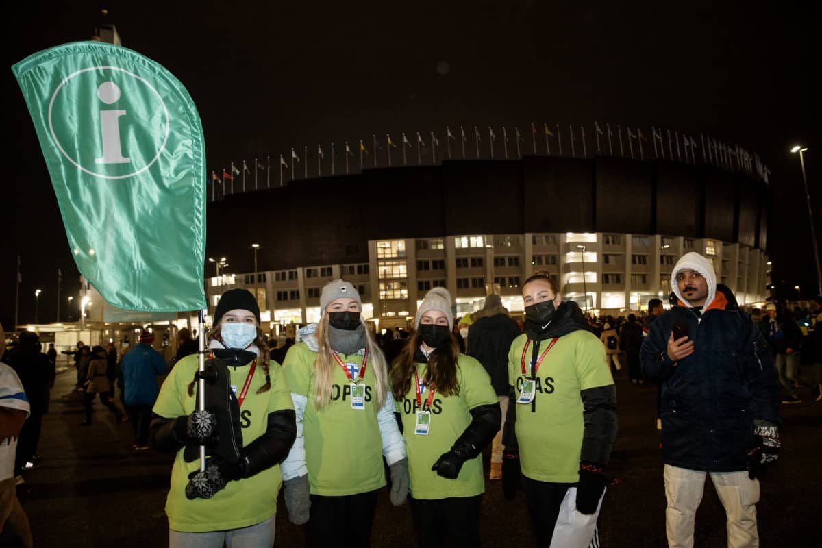 Vihreäpaitaisia oppaita Huuhkajien ottelussa Olympiastadionin ulkopuolella vihreän Info-kyltin kanssa.
