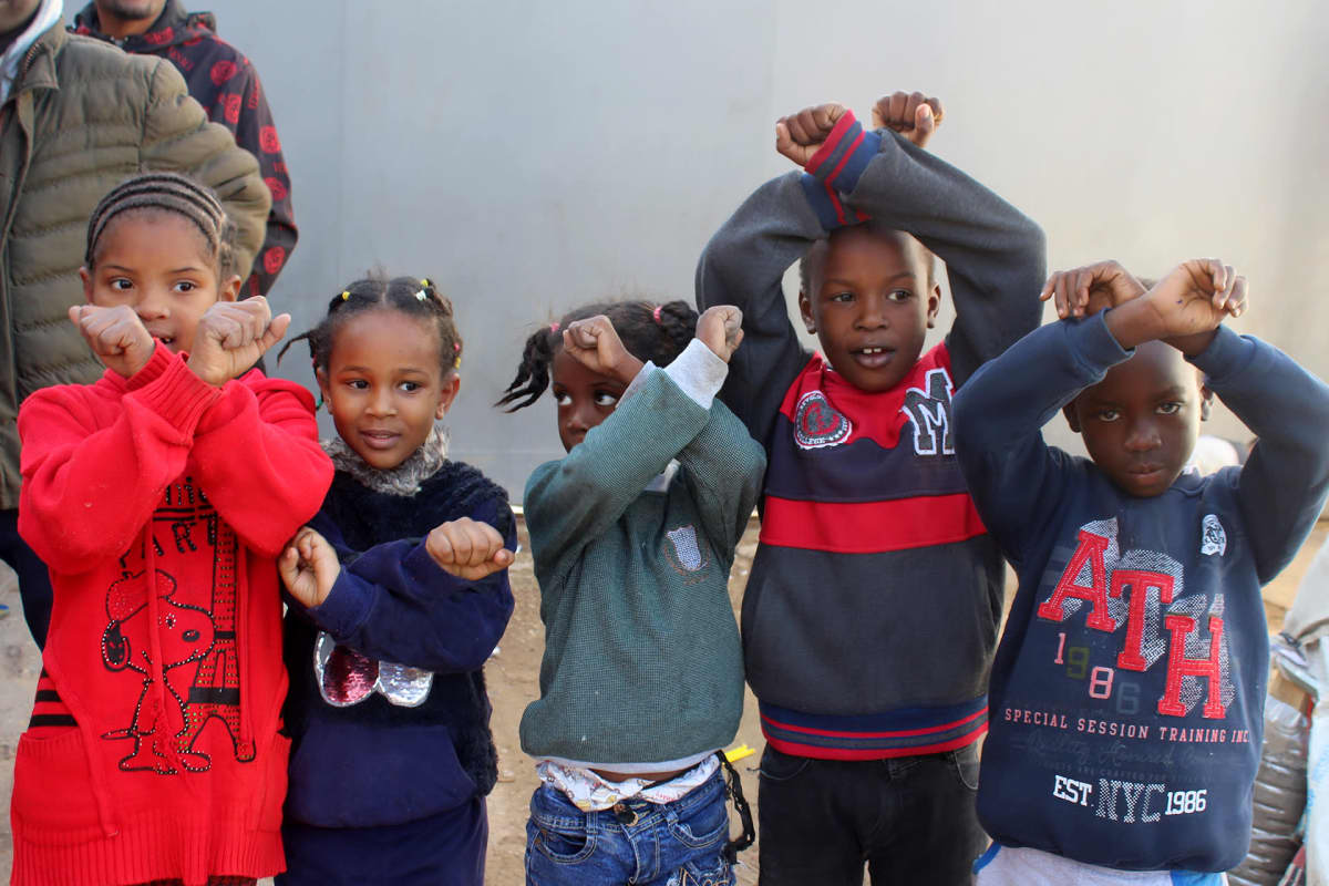 Lapset näyttävät käsimerkillä, että siirtolaisia pidätetään Libyassa.