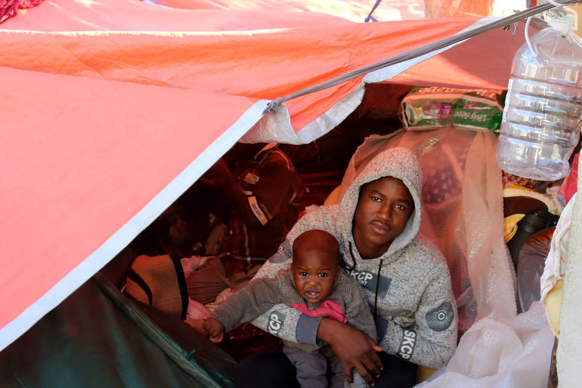 Mies ja lapsi katsovat kohti kameraa telttakankaan alta.