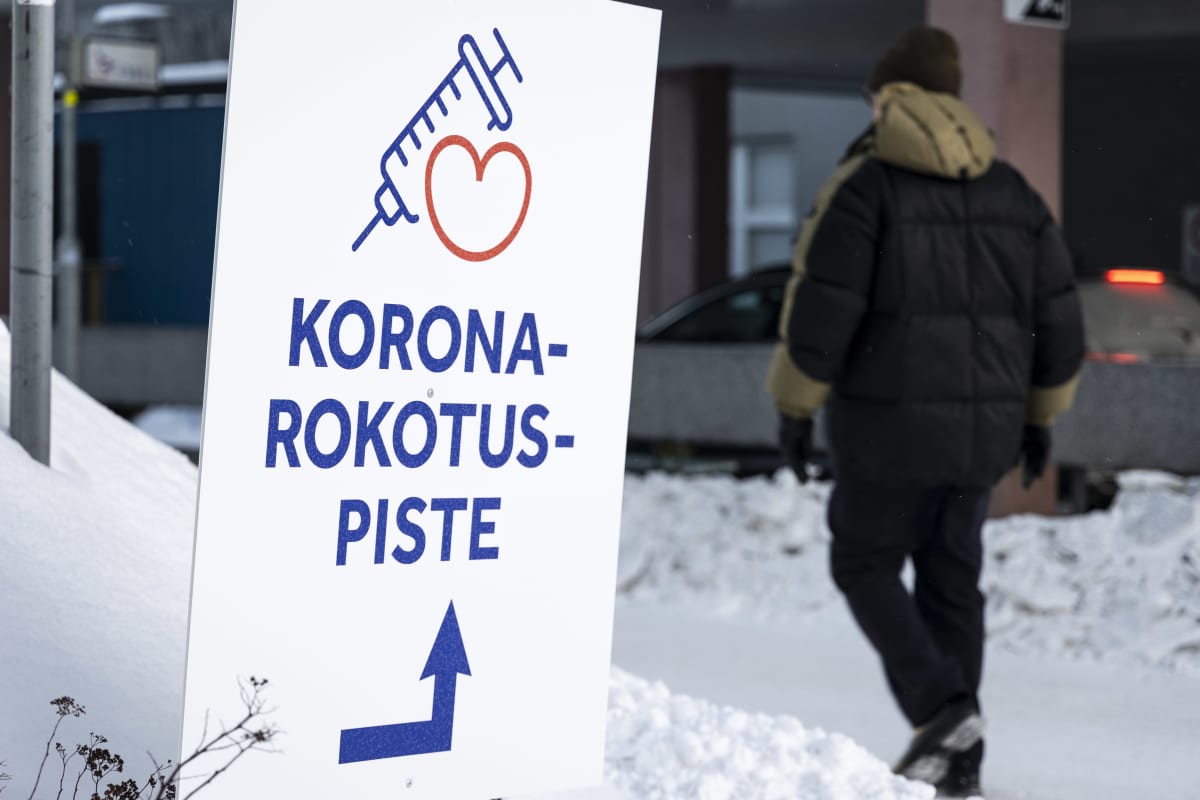Mies kävelee Kuopion pääterveysaseman edustalla, kuvan edessä kyltti jossa ohjeistetaan koronarokotuspisteelle.