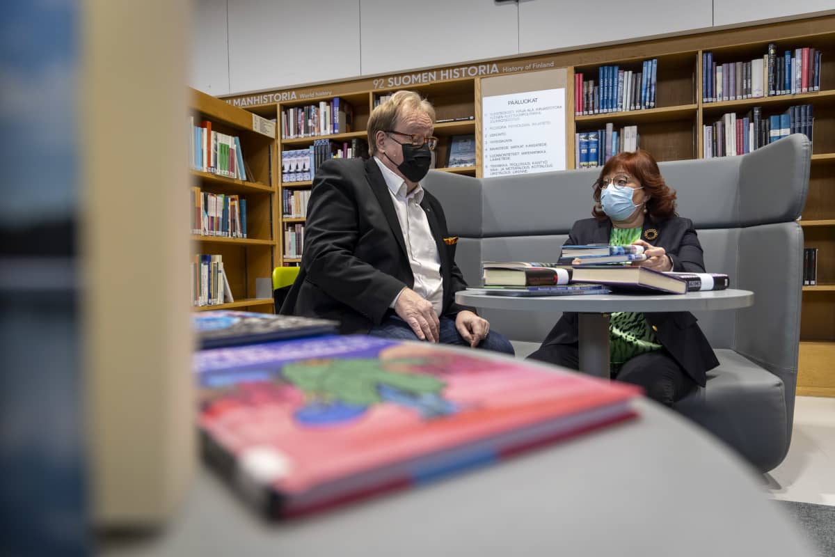 Jussi Tuovinen ja Varpu Puskala istuvat kirjojen peittämän pöydän ympärillä Kuopion kaupungin kirjastolla.