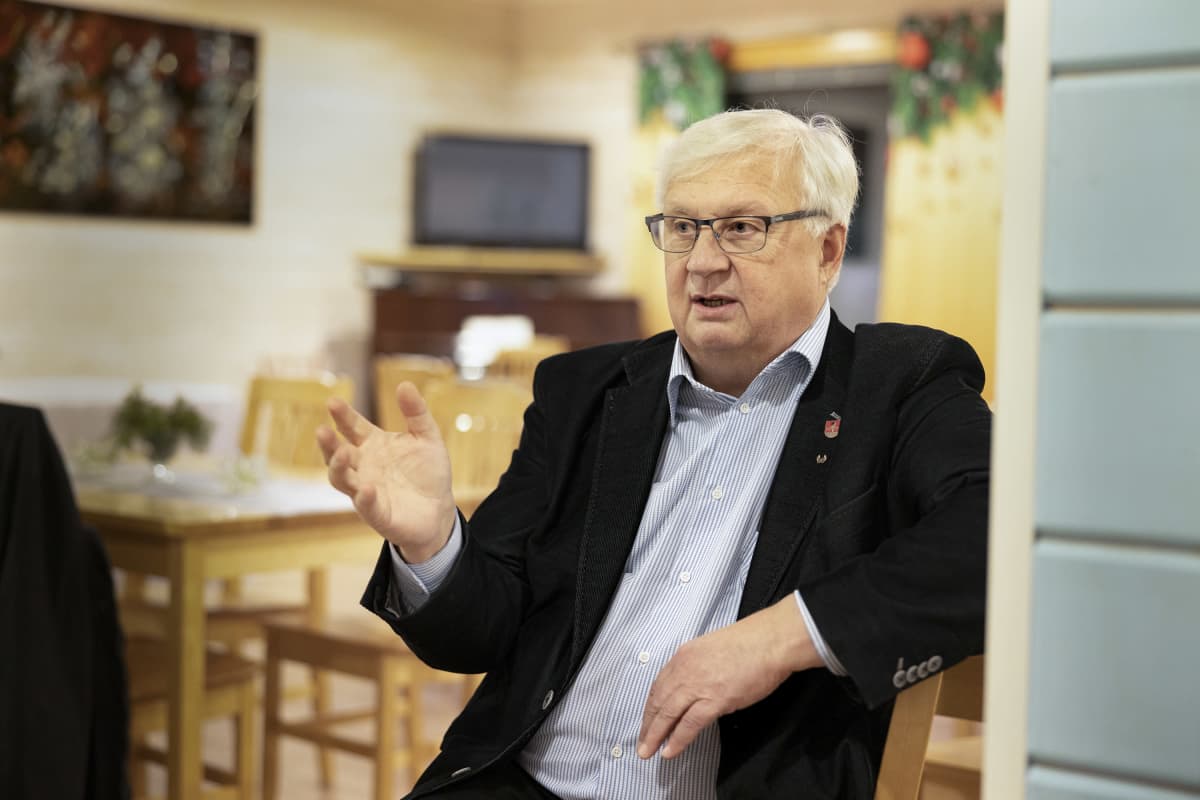 Pertti Huurtola istuu Karjalaisen kotileipomon juhlatilassa ja puhuu käsi heiluen.