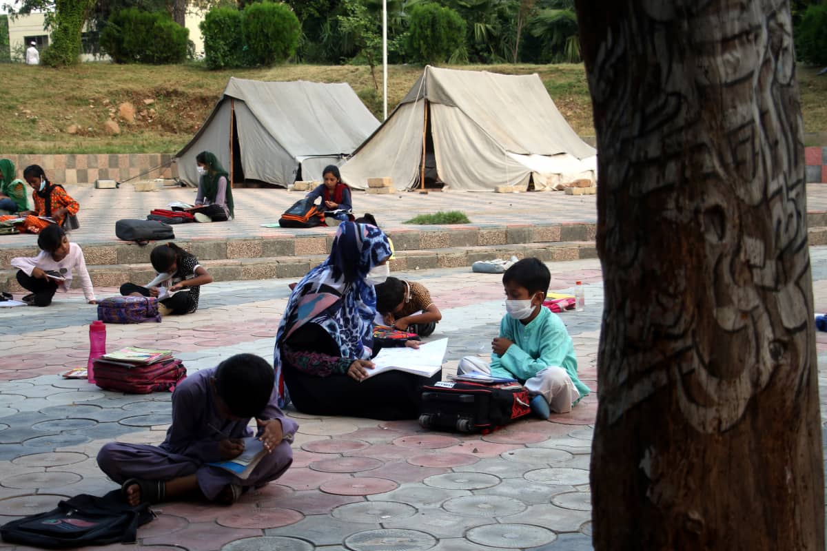 Ulkoilmakoulun oppitunnilla oppilaat istuvat maassa ja lukevat kirjoja toisistaan erillään Islamabadissa.