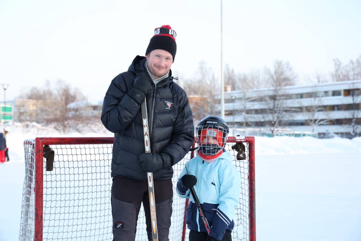 Isä ja poika seisovat jääkiekkomaalin edessä.