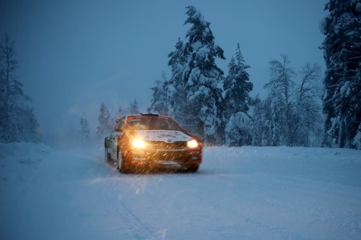 Ralliauto pimenevällä tiellä lumisateessa.