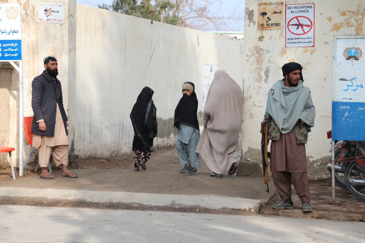 Aseistautunut mies ja ihmisiä seisoo terveyskeskuksen edessä Kandaharissa Afganistanissa.
