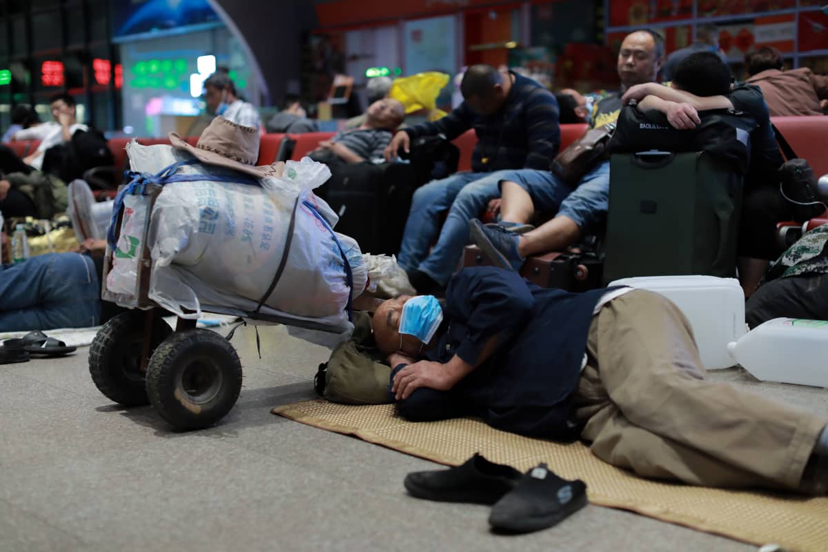 Mies nukkuu juna-aseman lattialla ohuen peiton päällä. Hänen vieressään on matkatavaroita pakattuna riisisäkkiin.