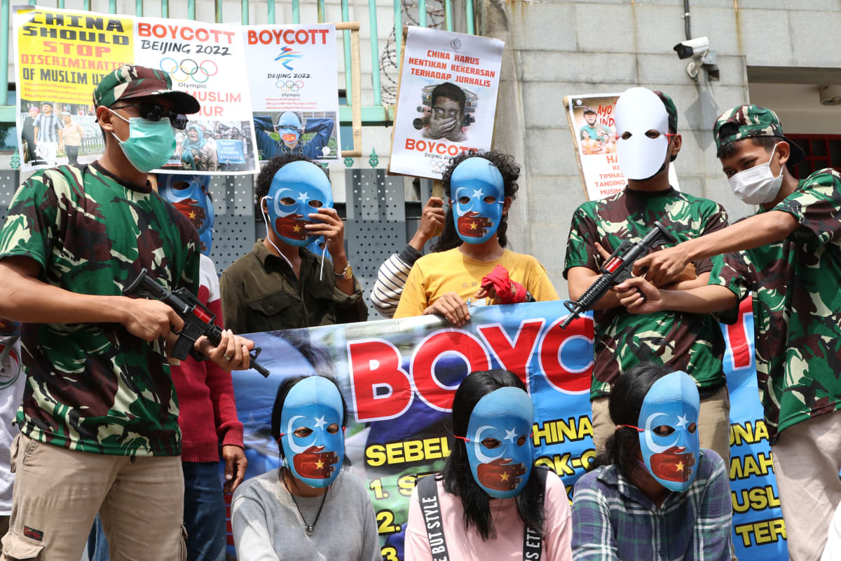 Mielenosoittajat vastustavat Pekingin olympialaisia. Heillä on kasvot peittävät siniset naamiot, sillä vaaleansininen väri viittaa uiguureihin. Osa on pukeutunut armeijakuosiin ja kantaa leikkiaseita.