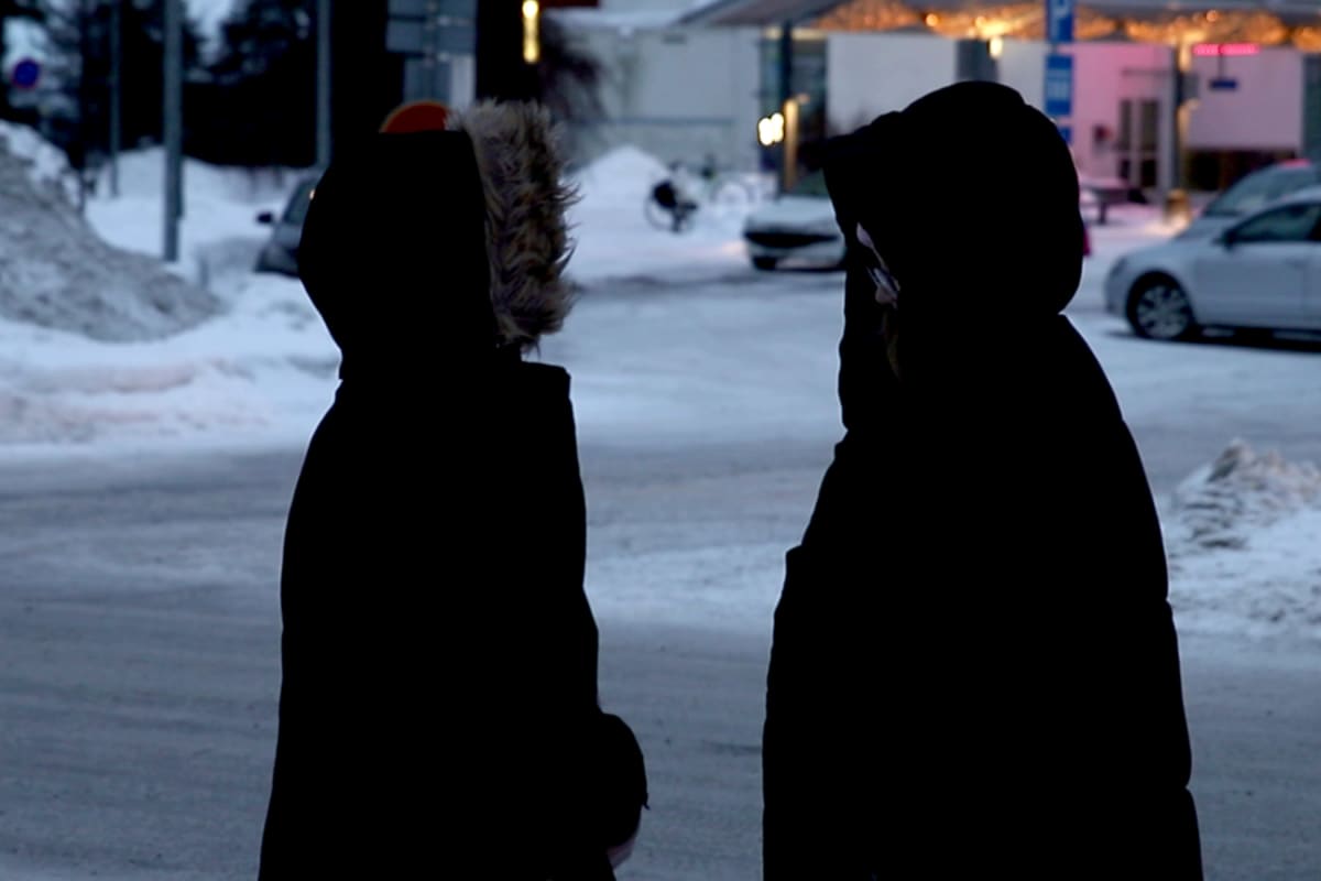 Kaksi mustiin talvivaatteisiin pukeutunutta nuorta keskustelee.