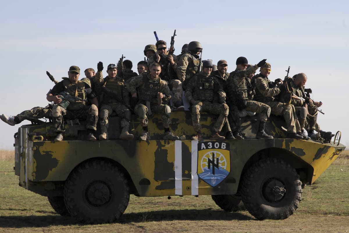 Iso joukko sotilaita istuu panssaroidun ajoneuvon päällä.