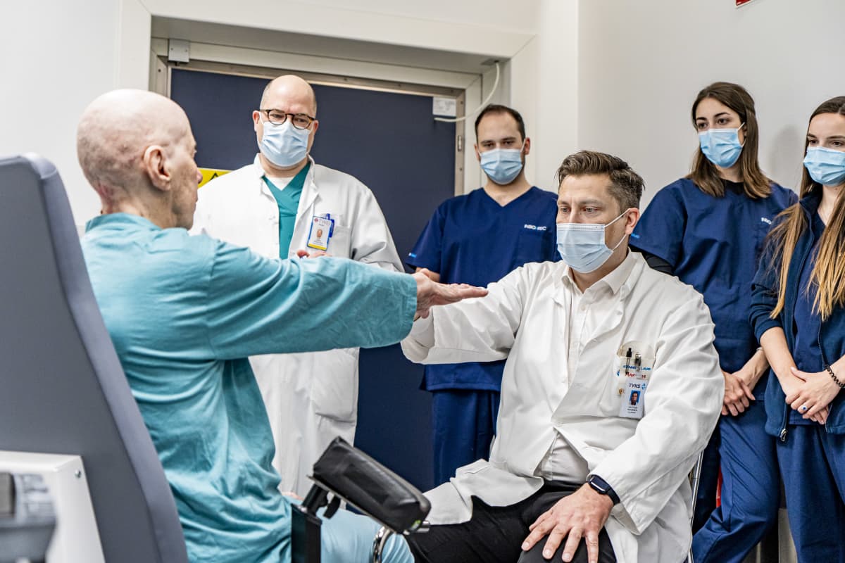 Potilas Marja Jalavanäyttää lääkäreille TYKSissä, miten hänen kätensä vapisevat.