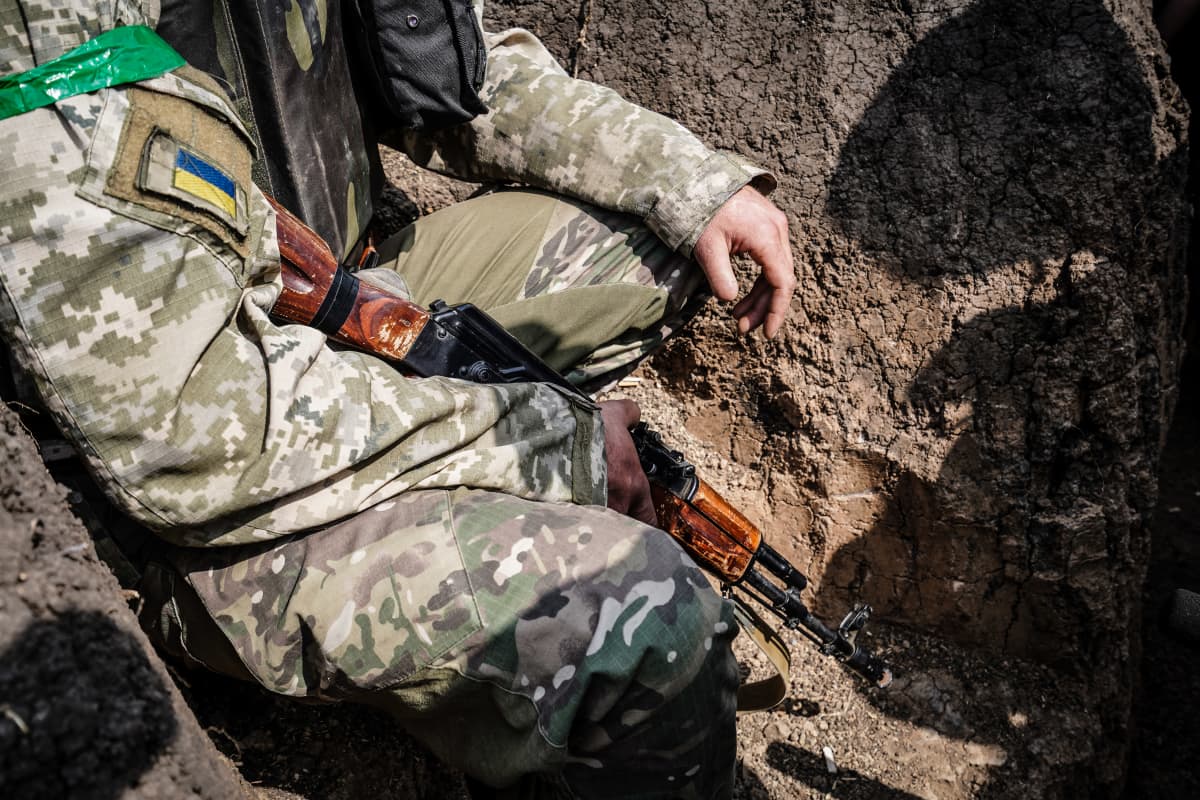 Ukrainalainen sotilas istuu ase kädessä juoksuhaudassa.