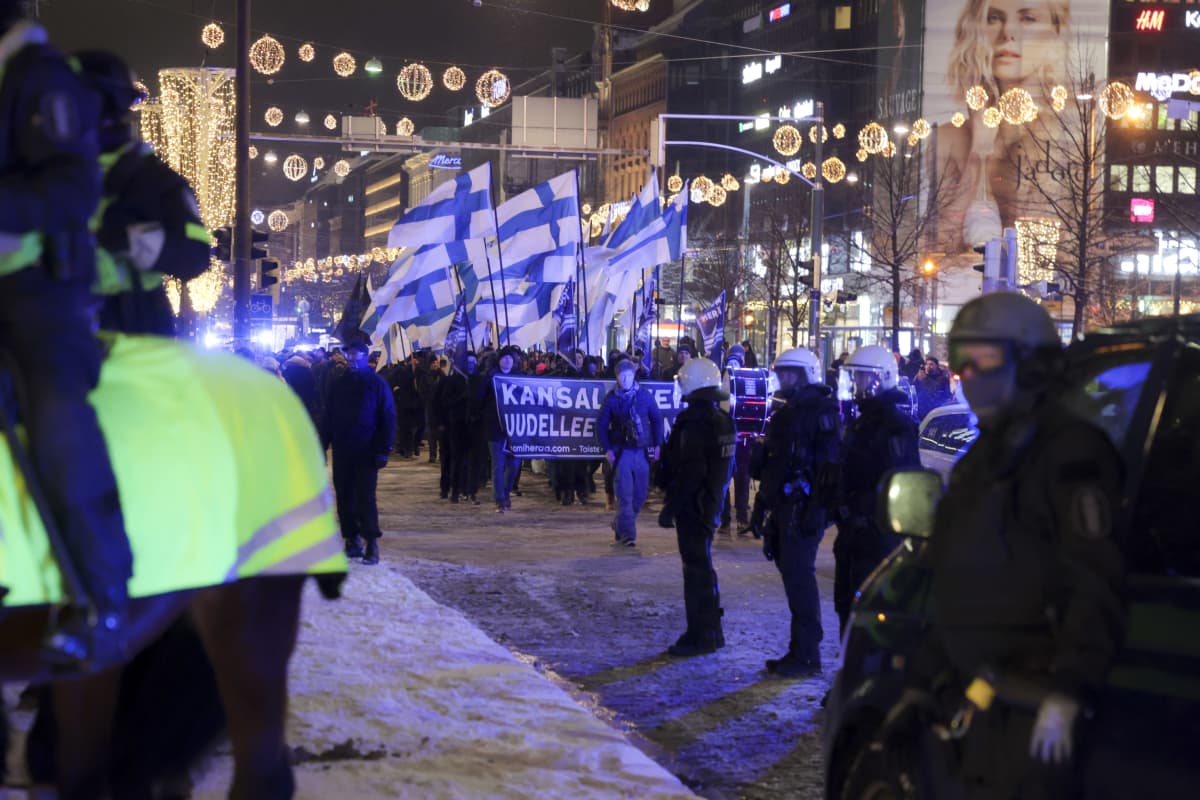 Suomi Herää -kulkue kulkee lumisessa maassa Suomenliput pystyssä. Poliisit valvovat.