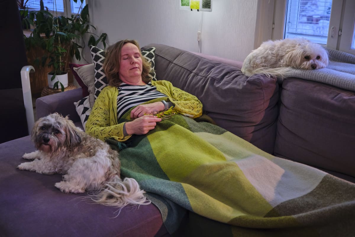 Tiina Peltola lepää sohvalla kahden koiransa kanssa.