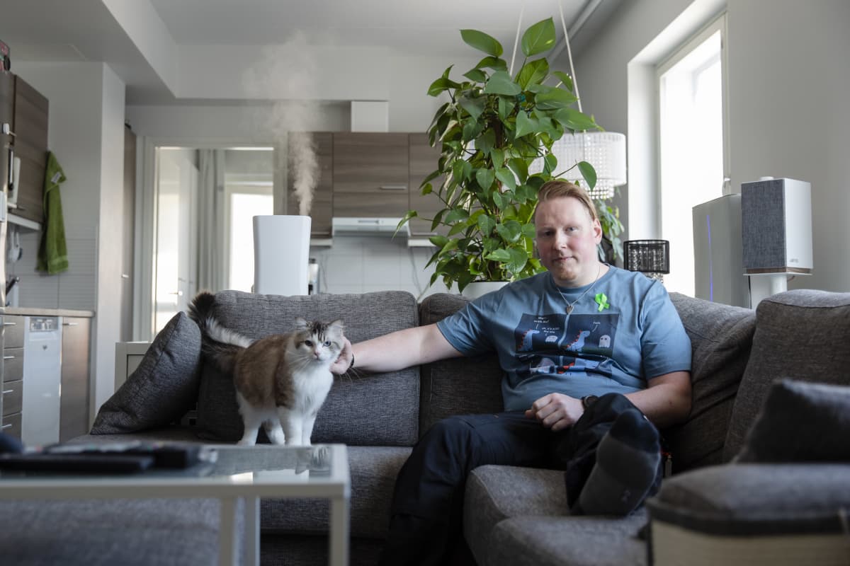 Mies ja kissa sohvalla katsovat kameraan. 