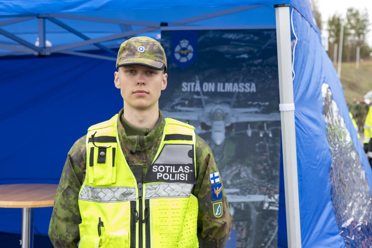 Suojausmies seisoo keltaisissa sotilaspoliisi-liiveissä sinisen teltan edessä.