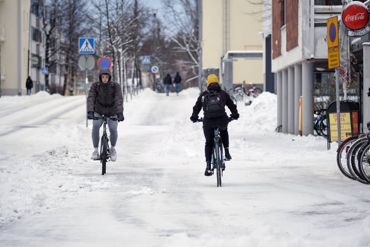 Kaksi pyöräilijää lumisella kadulla.