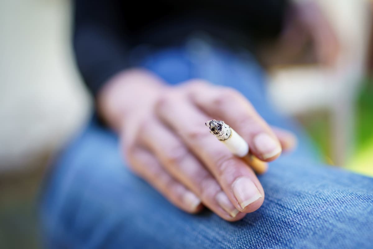 Naisen käsi, jossa sormien välissä palava savuke.