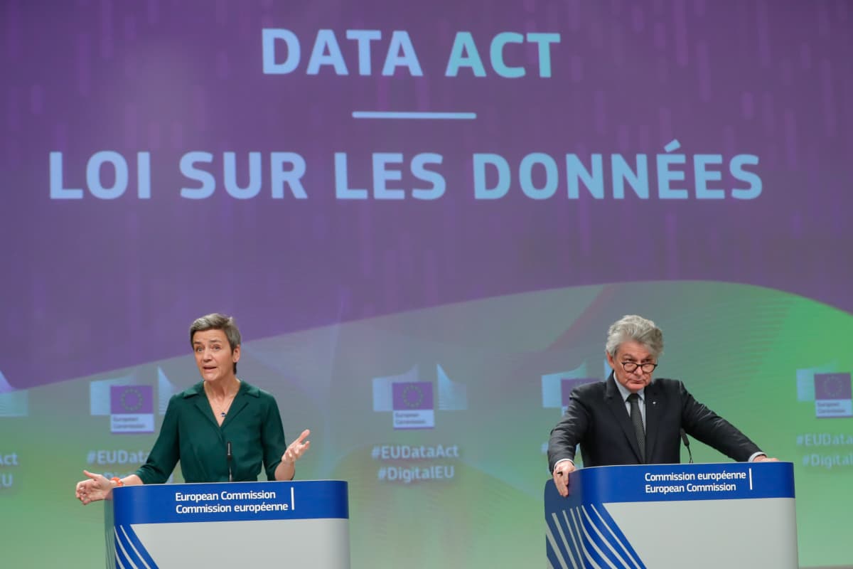 Vihreäpaitainen nainen levittelee käsiään vasemmalla, harmaantunut pukumies kuuntelee oikealla. Sinivihreällä taustalla lukee isolla: DATA ACT - LOI SUR LES DONNEES.