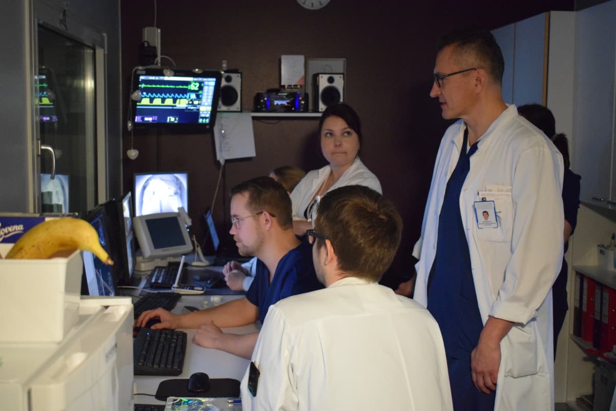 Tutkimusryhmä seuraa potilaan hoitoa valvomosta monitorien avulla.
