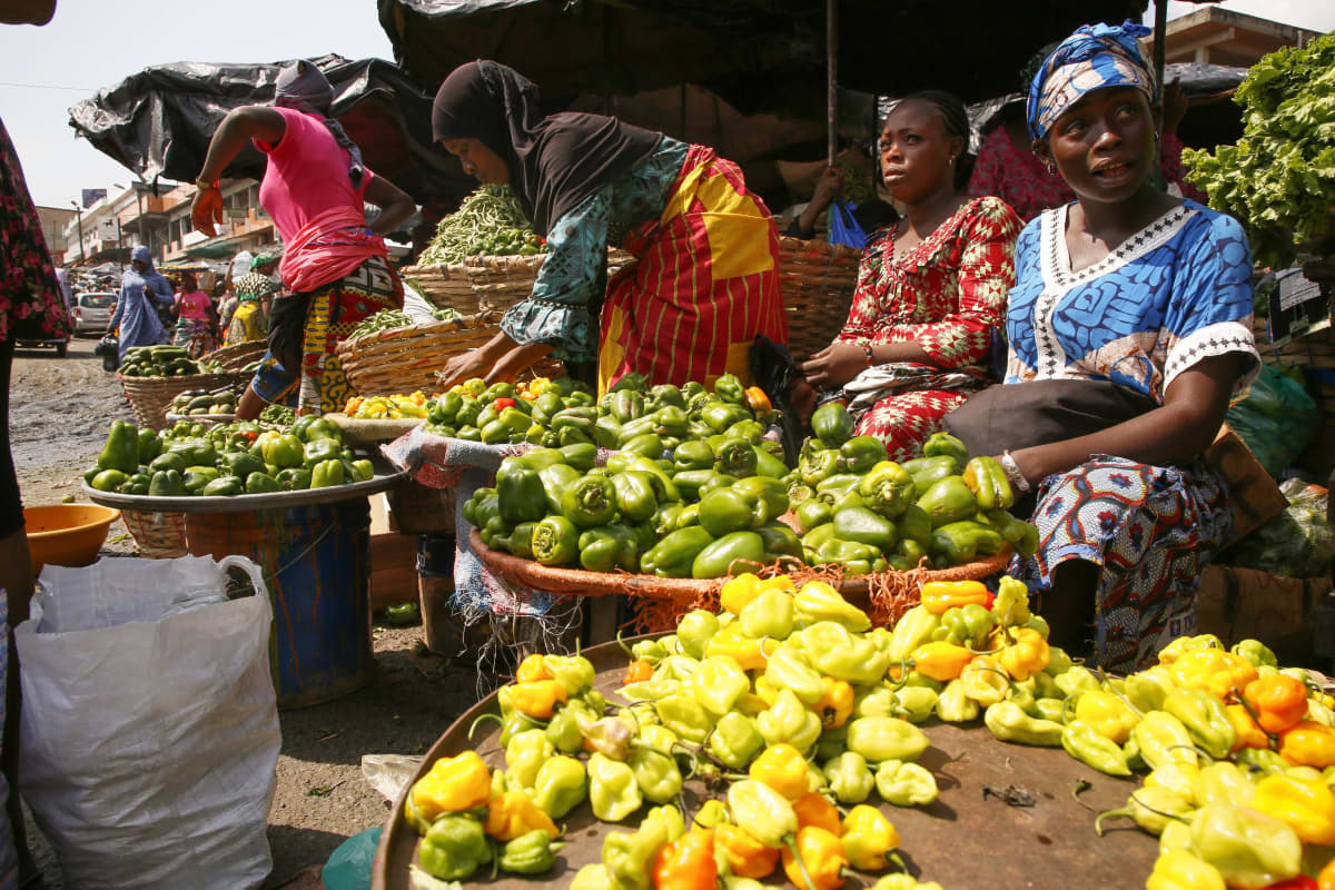 Kuvassa koreja, joissa on myynnissä olevia hedelmiä. Niiden takana istuu myyjiä. Kuva on otettu Abidjanissa Norsunluurannikolla. 
