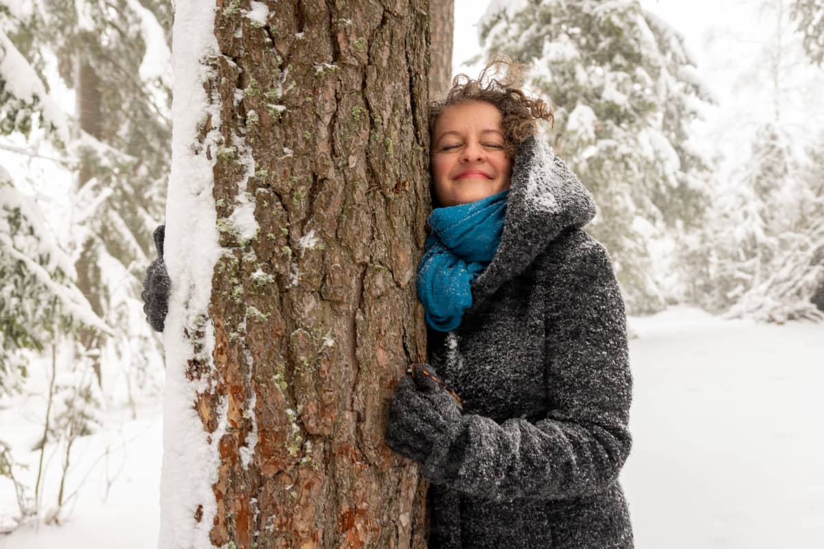 Stressivalmentaja Miia Huitti halaamassa mäntyä lumisessa maisemassa.