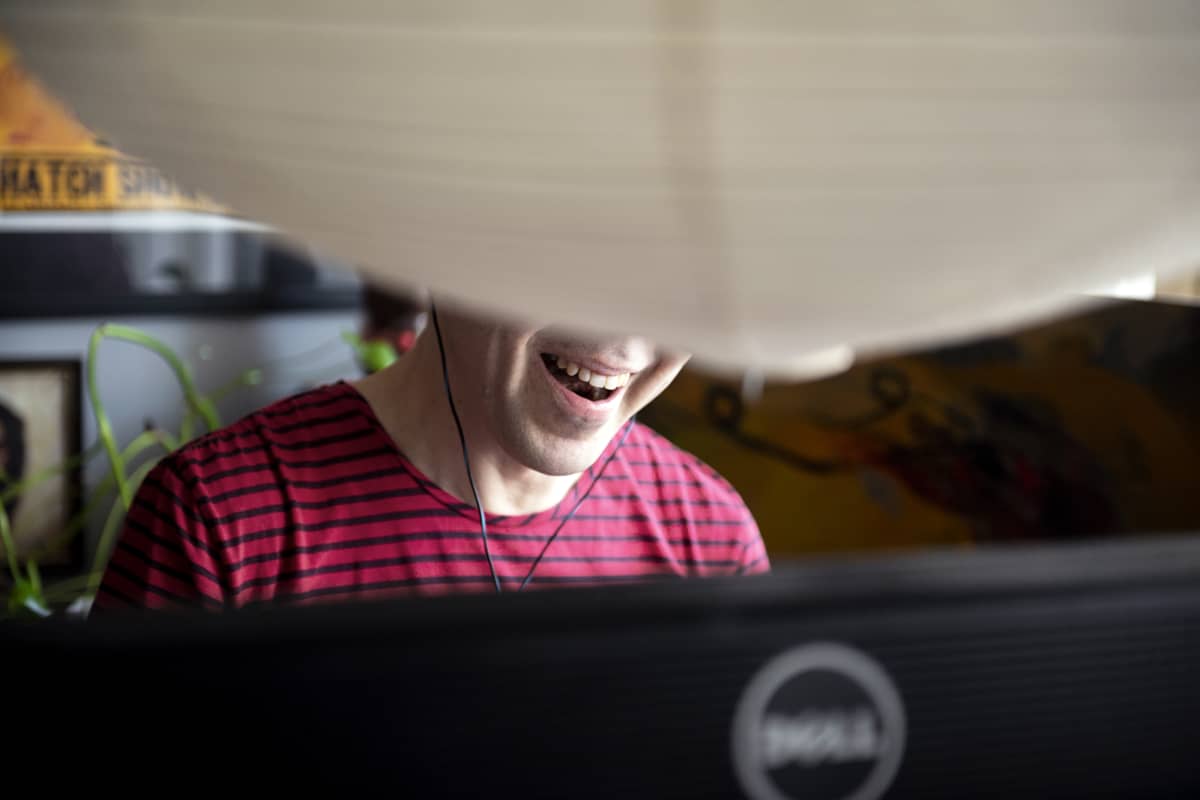 Mies nauraa tietokoneen ääressä kotonaan.