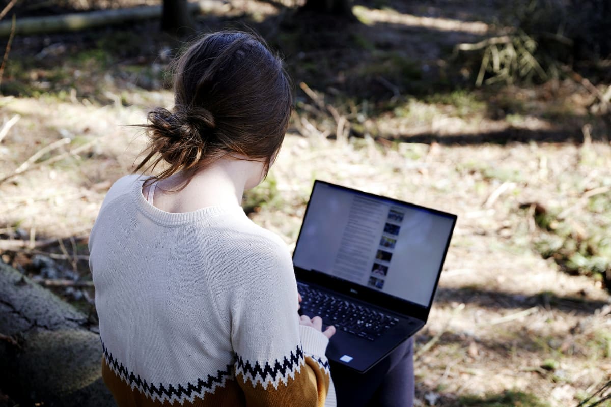 Kuvassa nainen tekee etätöitä tietokoneella metsässä.