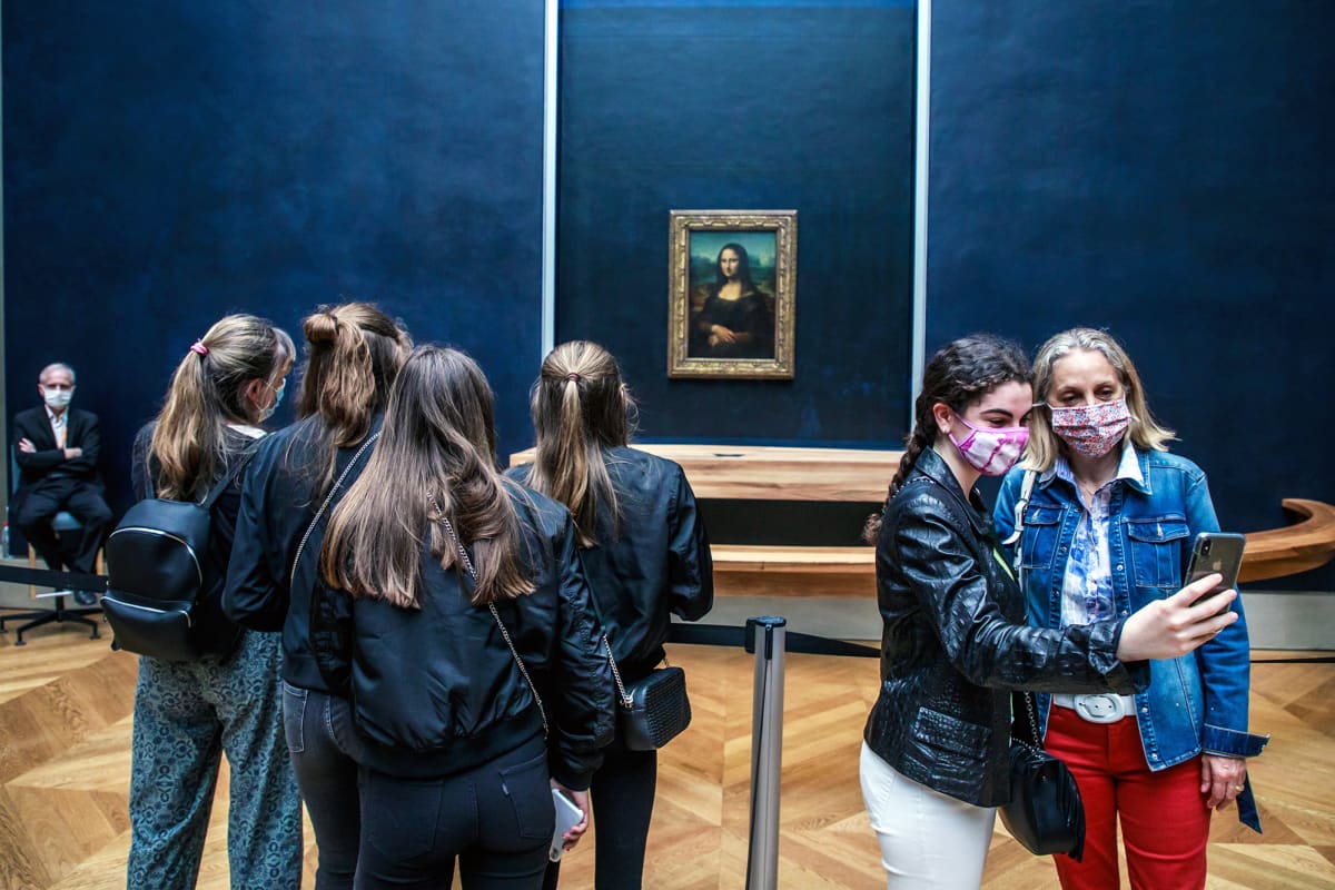 Museovieraa valokuvaavat itseään naista esittävän öljymaalauksen edessä Louvressa.