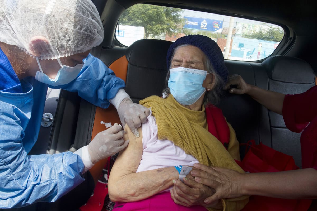 Sairaanhoitajat rokottavat vanhempaa naista auton sisällä.