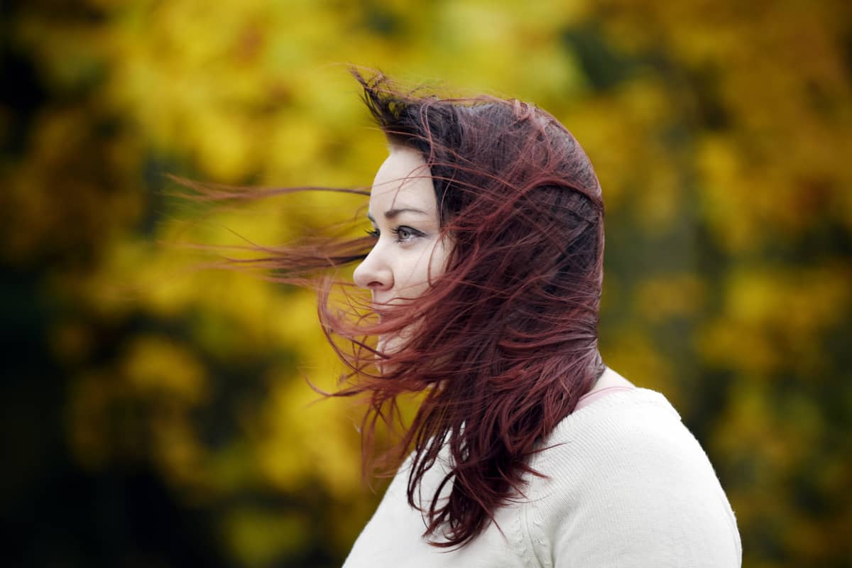 Nuori nainen seisoo hiukset hulmuten tuulessa.